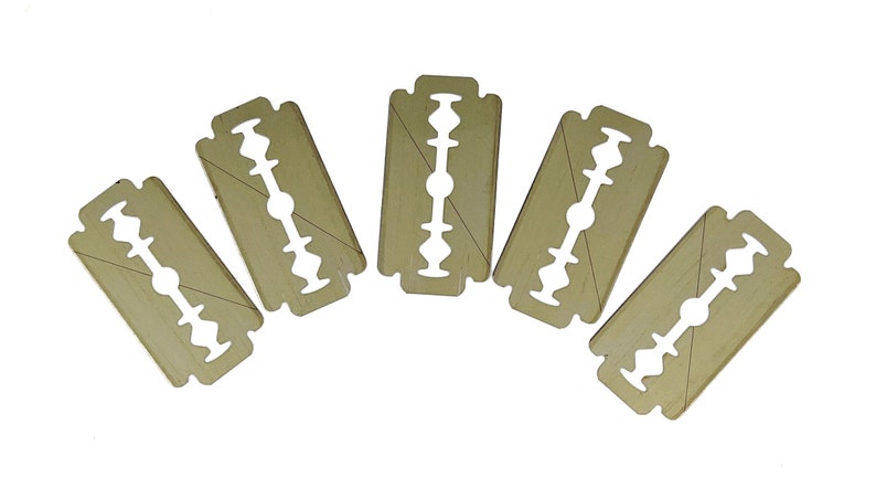 May include: Five gold-colored razor blades arranged in a semi-circle on a white background.