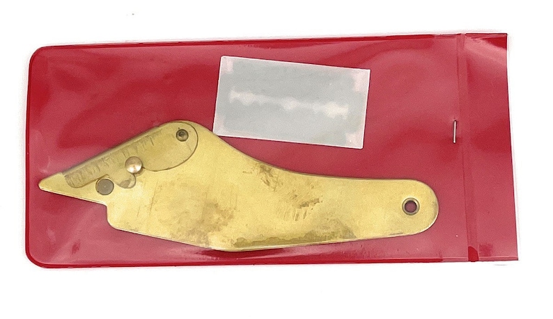 May include: A gold-colored metal tool with a curved shape and a small hole in the end. The tool is packaged in a red plastic bag.