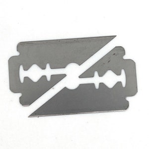 May include: A silver razor blade with a broken edge. The blade is designed with a central hole and a series of small holes along the edges.