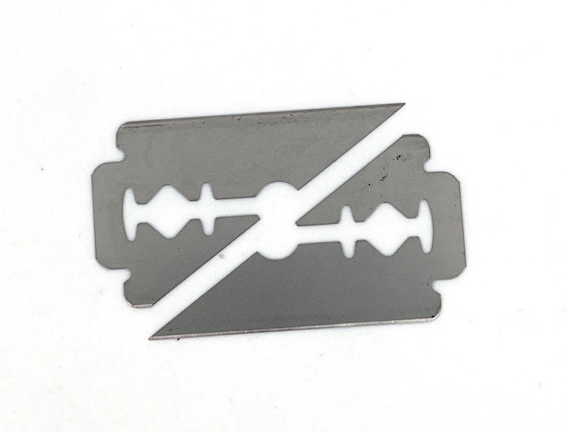 May include: A silver razor blade with a broken edge. The blade is designed with a central hole and a series of small holes along the edges.