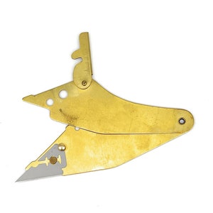 May include: A brass razor blade holder with a folding design. The holder has a small, sharp blade and a mechanism for adjusting the blade's position.