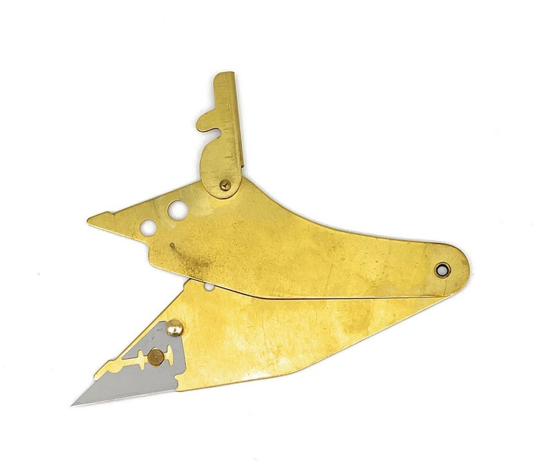 May include: A brass razor blade holder with a folding design. The holder has a small, sharp blade and a mechanism for adjusting the blade's position.