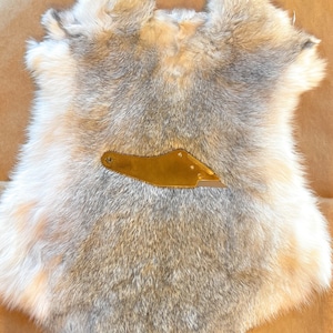 May include: A gray and white rabbit fur pelt with a small gold tool on top.