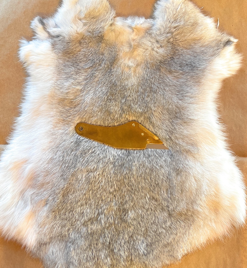 May include: A gray and white rabbit fur pelt with a small gold tool on top.