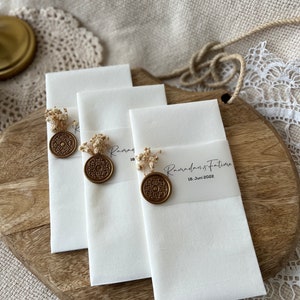 May include: Three white linen handkerchiefs with gold wax seals and dried flowers. The handkerchiefs have the text "Ramadan's Future 18. Juni 2022" printed on them.