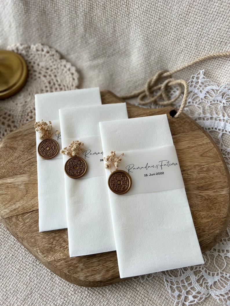 May include: Three white linen handkerchiefs with gold wax seals and dried flowers. The handkerchiefs have the text "Ramadan's Future 18. Juni 2022" printed on them.