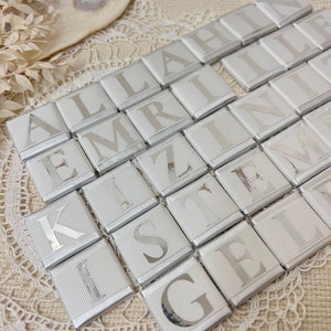 May include: Silver foil-wrapped chocolate squares with letters spelling out the phrase "ALLAHIN EMRINI KIZILIN ISTENEN GELIN"