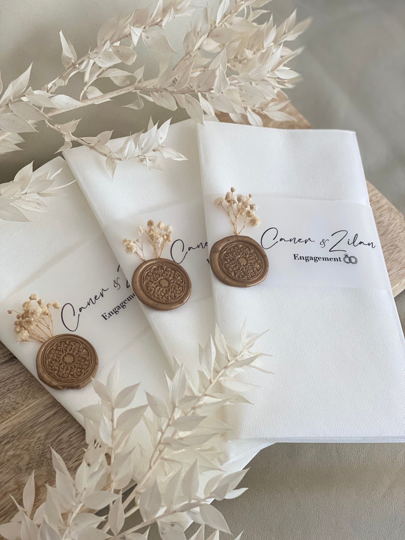 May include: Three white envelopes with gold wax seals and dried flowers. The envelopes are labeled with the text "Canen & Zilan Engagement".
