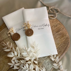 May include: Two white envelopes with gold wax seals and dried flowers. The envelopes have the text "Zehra & Mustafa" and "Aliyet olsun."