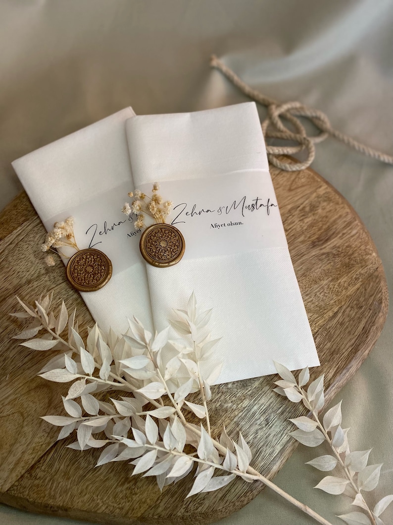 May include: Two white envelopes with gold wax seals and dried flowers. The envelopes have the text "Zehra & Mustafa" and "Aliyet olsun."