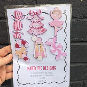 May include: A pack of pink and white Christmas-themed stickers. Designs include a Christmas tree, candy canes, a ballerina, and a nutcracker. The text "PARTY PIE DESIGNS" is printed on the bottom of the package.