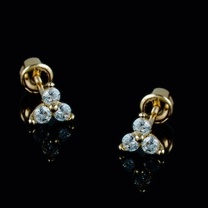 May include: A pair of gold stud earrings with three small, clear gemstones set in a triangular shape.