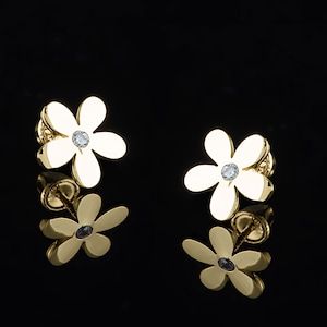 May include: A pair of gold flower-shaped earrings with a single clear rhinestone in the center of each flower.