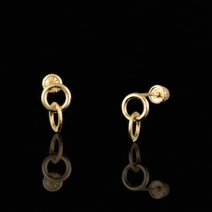 May include: A pair of gold-toned earrings with a double circle design. The earrings are made of metal and have a post back closure.