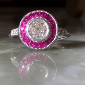 Puede incluir: Un anillo de plata con un gran diamante redondo rodeado por un halo de rubíes rosas.