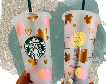 May include: Clear plastic Starbucks cold cup with a green straw. The cup is decorated with gold maple leaves, hearts, and gradient pink pumpkins. The Starbucks logo is in green. The cup is designed for cold beverages.