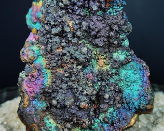 May include: A large, iridescent rock with a rough, textured surface. The rock is covered in small, round bumps and has a variety of colors, including blue, green, purple, and red.