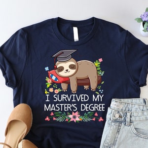 May include: A navy blue t-shirt with a cartoon sloth wearing a graduation cap and holding a diploma. The shirt has the text "I survived my master's degree" with floral accents.