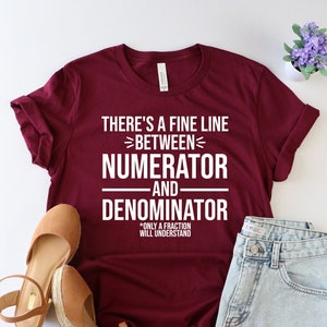 May include: A maroon t-shirt with white text that reads "There's a fine line between numerator and denominator. Only a fraction will understand."