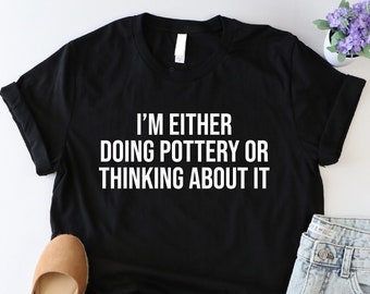 May include: Black t-shirt with white text that reads "I'm either doing pottery or thinking about it."