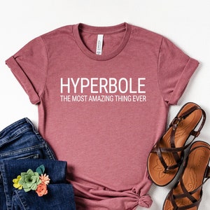 May include: A mauve t-shirt with the text "HYPERBOLE THE MOST AMAZING THING EVER" in white lettering.