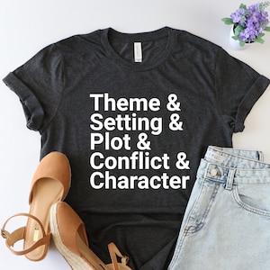 Pu&ograve; includere: Una maglietta grigia scura con il testo "Theme & Setting & Plot & Conflict & Character" stampato in bianco.