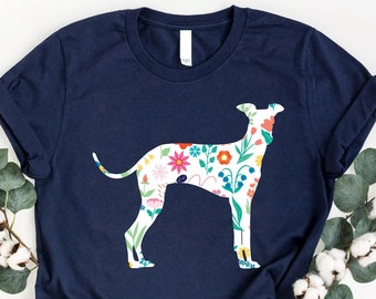 May include: A navy blue t-shirt with a floral patterned silhouette of a dog. The shirt is laid flat on a white background with eucalyptus branches and cotton bolls.