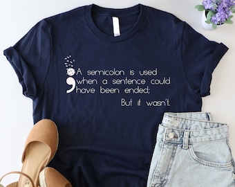 May include: A navy blue t-shirt with a white semicolon and the text "A semicolon is used when a sentence could have been ended: But it wasn't."