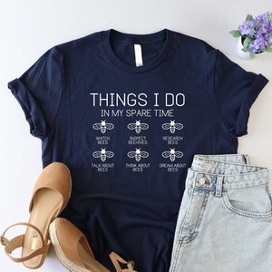 May include: A navy blue t-shirt with the text "THINGS I DO IN MY SPARE TIME" and a list of bee-related activities: "WATCH BEES", "INSPECT BEEHIVES", "RESEARCH BEES", "TALK ABOUT BEES", "THINK ABOUT BEES", and "DREAM ABOUT BEES".