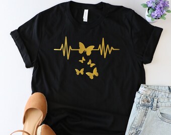May include: Black t-shirt with a gold heartbeat graphic and butterflies. The graphic features a stylized heartbeat with five butterflies flying around it.
