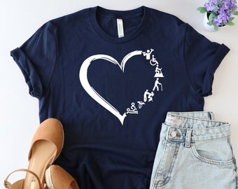May include: A navy blue t-shirt with a white heart design. The heart is filled with white silhouettes of people in various stages of mobility, including a person in a wheelchair, a person using crutches, and a person walking with a cane.