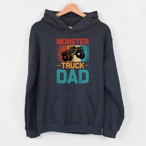 May include: A dark blue hooded sweatshirt with a vintage-style graphic of a monster truck and the text "Monster Truck Dad".