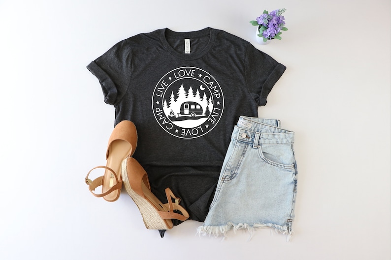 May include: A dark gray t-shirt with a white circle graphic featuring a camper, trees, and the text "Live * Love * Camp * Live * Love * Camp".