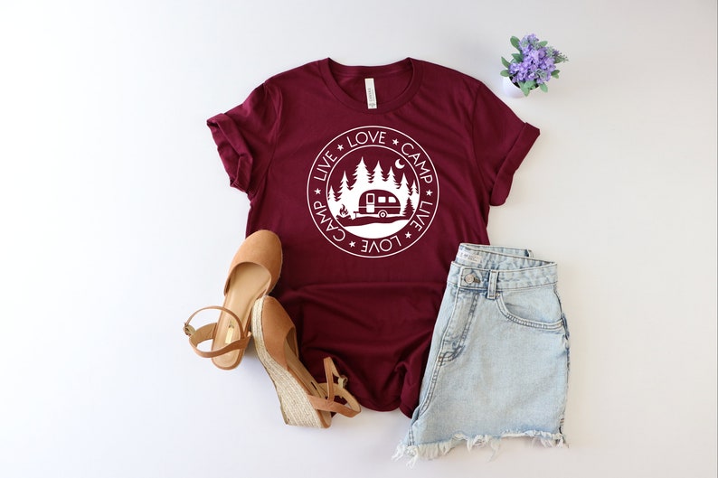 May include: A maroon t-shirt with a white circle graphic featuring a camper, trees, and the text "Live * Love * Camp * Live * Love * Camp".