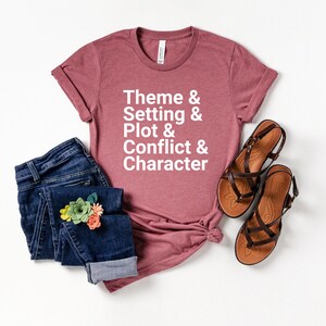 Pu&ograve; includere: Una maglietta color malva con il testo "Theme & Setting & Plot & Conflict & Character" in lettere bianche.