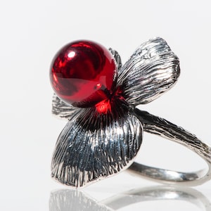 Op de afbeelding: Een zilveren ring met een rode edelsteen in de vorm van een bloem.