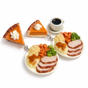 May include: A set of miniature food charms featuring two slices of orange pumpkin pie with white whipped cream, two white plates with sliced meat, mashed potatoes with gravy, carrots, and broccoli, and a small white cup of black coffee.