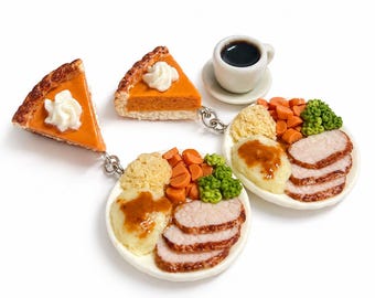 Puede incluir: Un conjunto de dijes de comida en miniatura que incluye dos rebanadas de pastel de calabaza naranja con crema batida blanca, dos platos blancos con carne en rodajas, puré de patatas con salsa, zanahorias, brócoli y una taza de café negro.