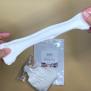 May include: A white air-dry clay being stretched and pulled apart. The clay is packaged in a clear plastic bag with a white label that reads "KMC Air-Dry Clay".