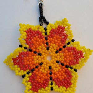 Puede incluir: Un pendiente de estrella con cuentas de color amarillo, naranja y rojo degradado. El centro de la estrella tiene un patr&oacute;n de cuentas negras.