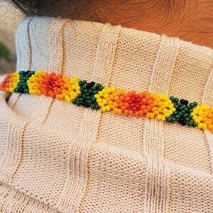 Puede incluir: Primer plano de un collar de cuentas con cuentas verdes, amarillas, naranjas y rojas. El collar lo lleva una persona con cabello casta&ntilde;o.