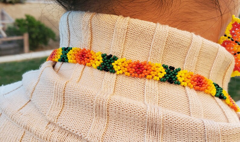 Puede incluir: Primer plano de un collar de cuentas con cuentas verdes, amarillas, naranjas y rojas. El collar lo lleva una persona con cabello casta&ntilde;o.