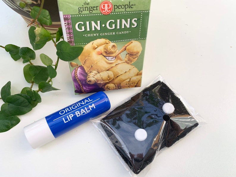 May include: A blue lip balm tube with the words "ORIGINAL LIP BALM" printed on it.  The lip balm is next to a black cloth face mask with two white buttons.  A box of "GIN-GINS CHEWY GINGER CANDY" is in the background.