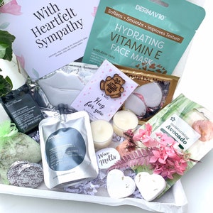May include: A white gift box filled with self-care items, including a face mask, bath bombs, candles, and a wooden heart with the text "A big hug for you". The box also includes a card with the text "With Heartfelt Sympathy".