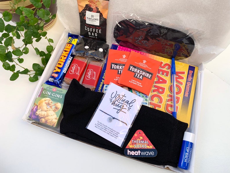 May include: A gift box filled with various items, including a chocolate bar, tea bags, a book, socks, a lip balm, and a bracelet. The box also includes a card that says "Virtual hug".