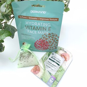 May include: Two face masks, one with a green and white design and the text "Moisturizing Avocado Face Mask" and the other with a blue and gold design and the text "Hydrating Vitamin E Face Mask with Aloe Vera".