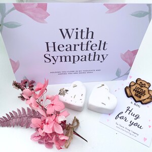 May include: A sympathy gift set with a card that reads "With Heartfelt Sympathy", two white heart-shaped bath bombs, a small wooden bear charm with the text "Little Pocket Hug", and a card that reads "A Big Hug for You".