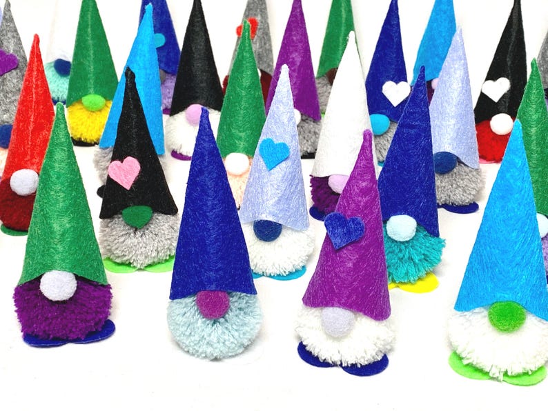 May include: A collection of colorful gnome figurines with cone-shaped hats in various colors, including green, blue, purple, and black. Each gnome has a fluffy beard and a small heart or white heart-shaped accent on the hat. The gnomes are standing on a white surface.