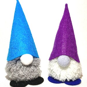 May include: Two handmade gnome figurines. One gnome has a blue felt hat, gray beard, white nose, and black shoes. The other has a purple hat, white beard, gray nose, and blue shoes. These decorative gnomes are perfect for home decor.