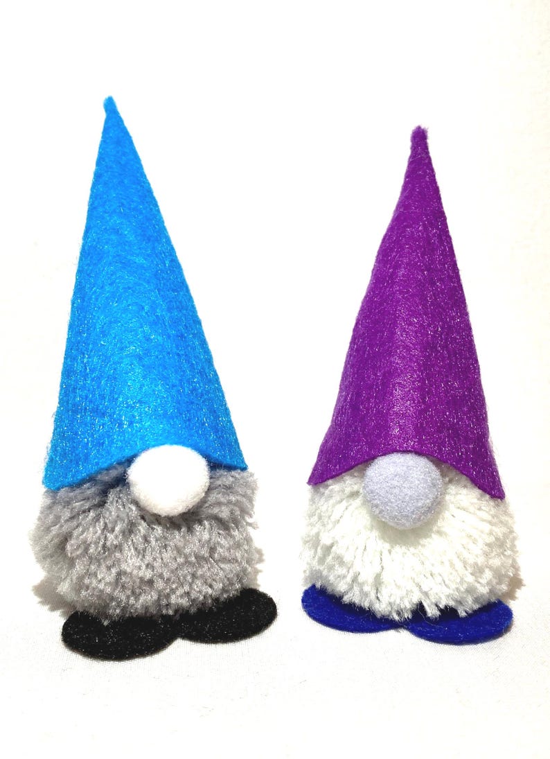 May include: Two handmade gnome figurines. One gnome has a blue felt hat, gray beard, white nose, and black shoes. The other has a purple hat, white beard, gray nose, and blue shoes. These decorative gnomes are perfect for home decor.